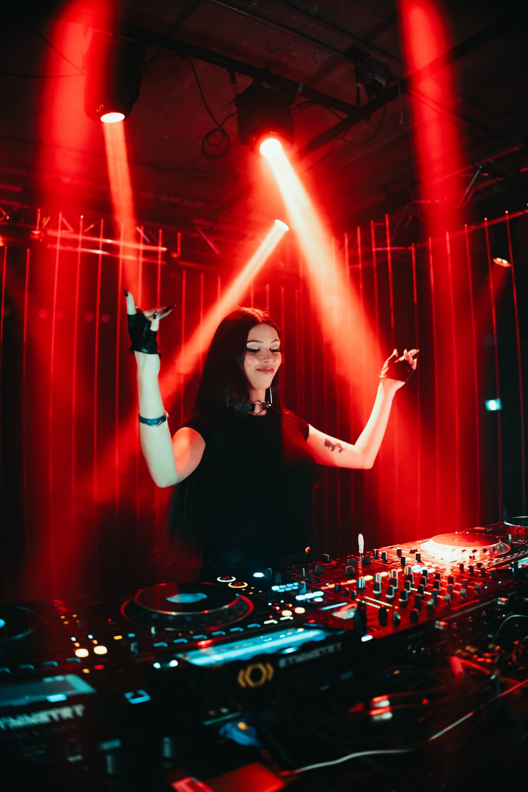 ELL3NI behind the decks with arms raised under red stage lighting